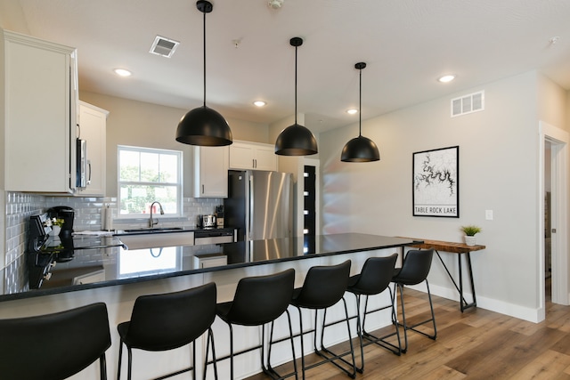 kitchen with pendant lighting, sink, white cabinetry, stainless steel appliances, and light hardwood / wood-style floors