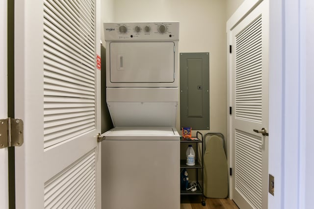 clothes washing area featuring wood-type flooring, electric panel, and stacked washer and dryer