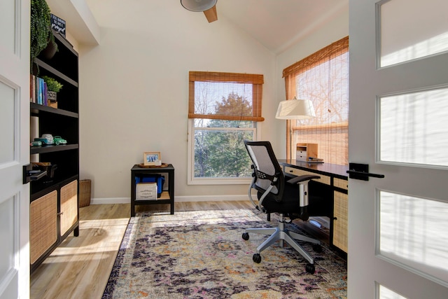 home office with a wealth of natural light, vaulted ceiling, and light hardwood / wood-style floors