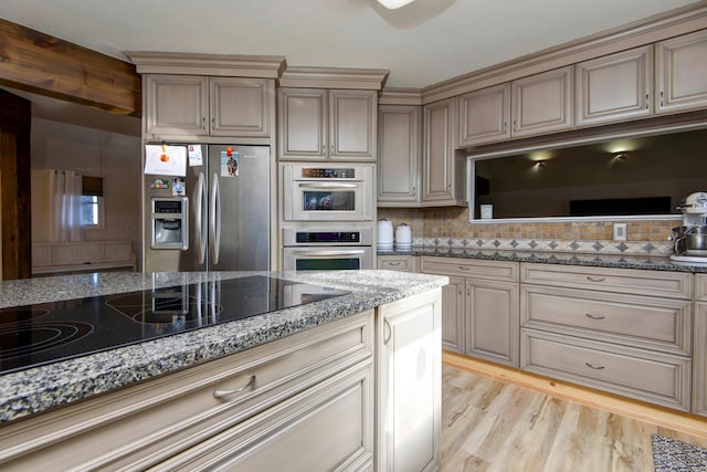 kitchen with light hardwood / wood-style floors, stone counters, decorative backsplash, and stainless steel appliances