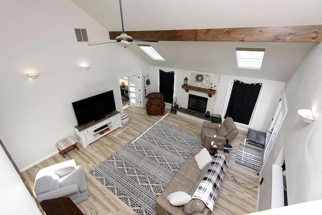 living room featuring a skylight, a brick fireplace, high vaulted ceiling, and light hardwood / wood-style floors