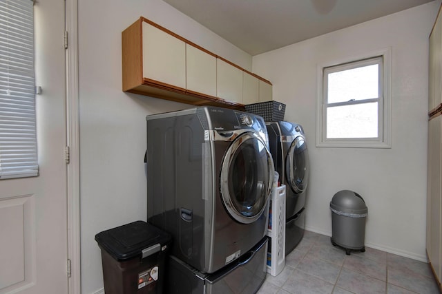 clothes washing area featuring washing machine and clothes dryer, light tile patterned floors, and cabinets