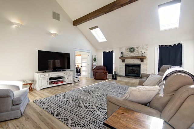 living room featuring a brick fireplace, high vaulted ceiling, beamed ceiling, light hardwood / wood-style floors, and a skylight