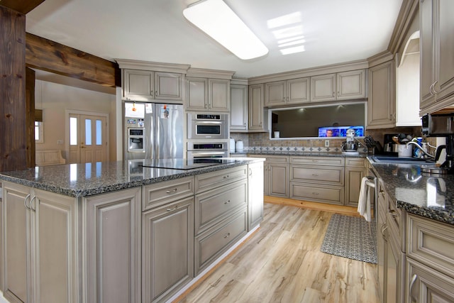 kitchen featuring sink, dark stone counters, light hardwood / wood-style flooring, appliances with stainless steel finishes, and backsplash