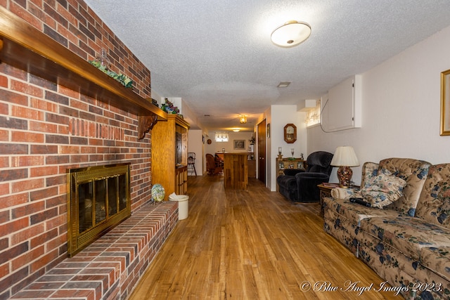 unfurnished living room featuring hardwood / wood-style flooring, a brick fireplace, brick wall, and a textured ceiling