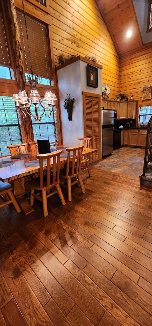 dining room with high vaulted ceiling, wood ceiling, a notable chandelier, light hardwood / wood-style flooring, and wood walls