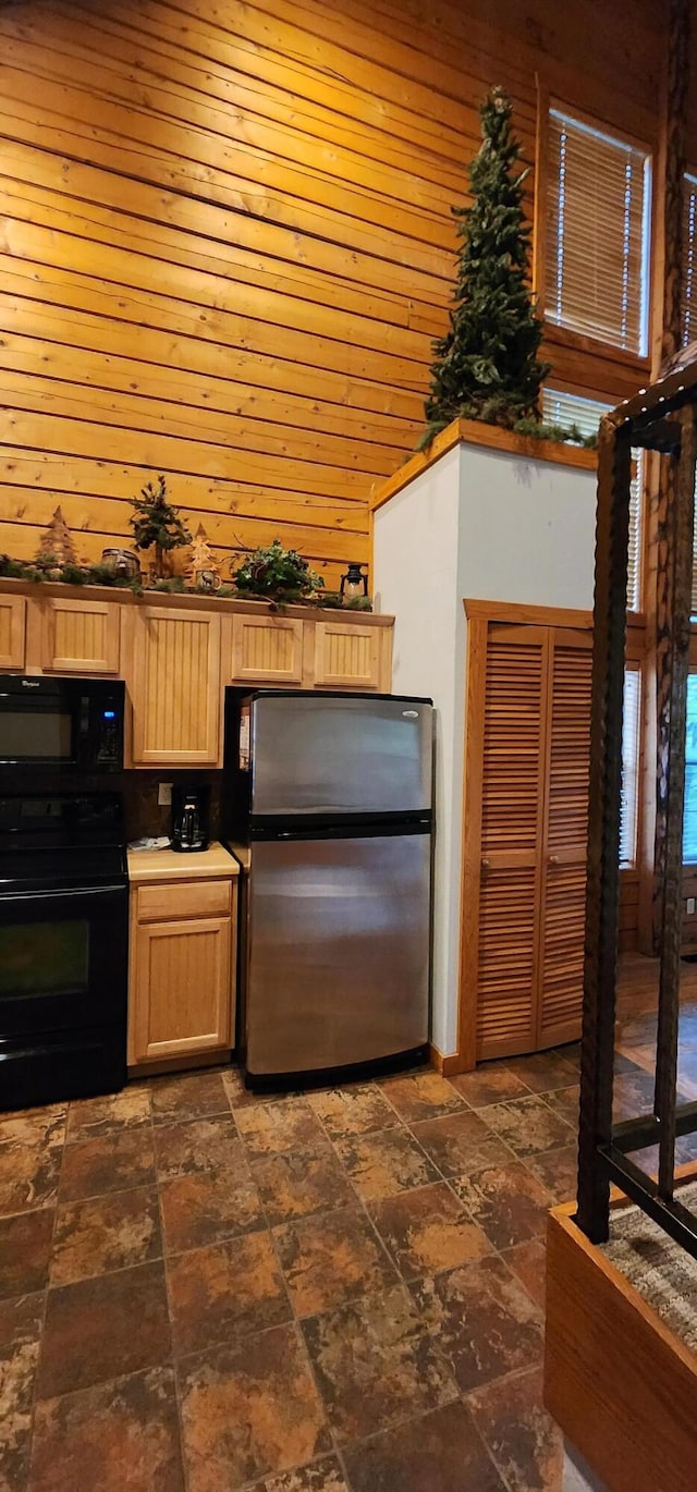 kitchen featuring light brown cabinets, wooden walls, and black appliances