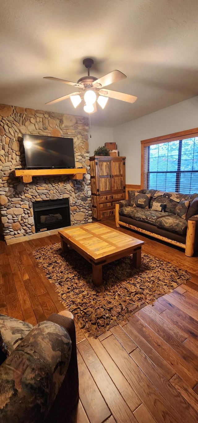 living room featuring ceiling fan, a stone fireplace, and hardwood / wood-style flooring