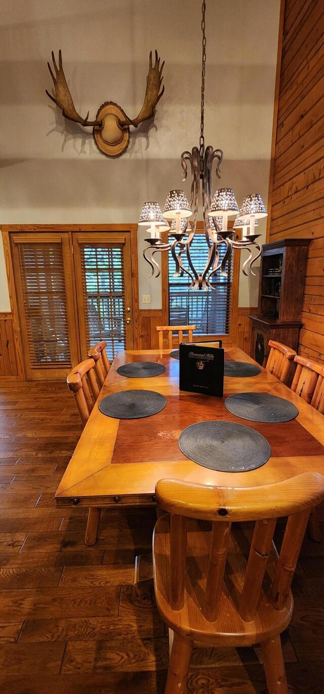 dining room with dark hardwood / wood-style floors, wooden walls, a high ceiling, and a chandelier