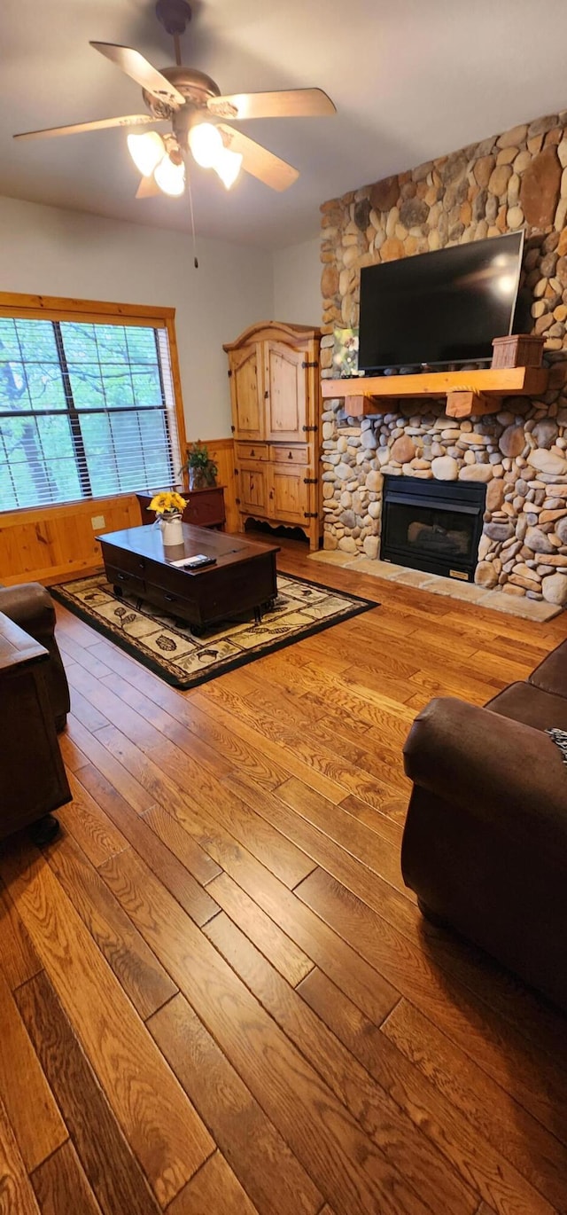 living room featuring hardwood / wood-style flooring, ceiling fan, and a stone fireplace