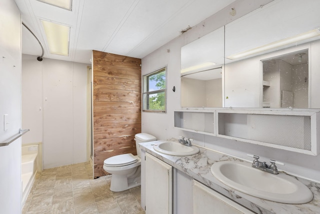 bathroom with a tub, vanity, wood walls, and toilet