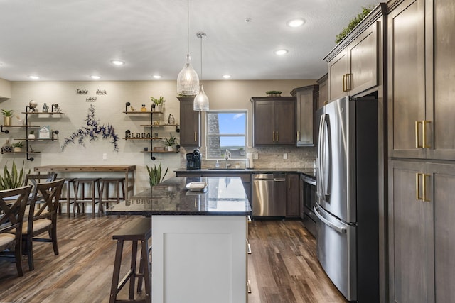 kitchen with dark brown cabinets, dark stone counters, tasteful backsplash, appliances with stainless steel finishes, and a breakfast bar area