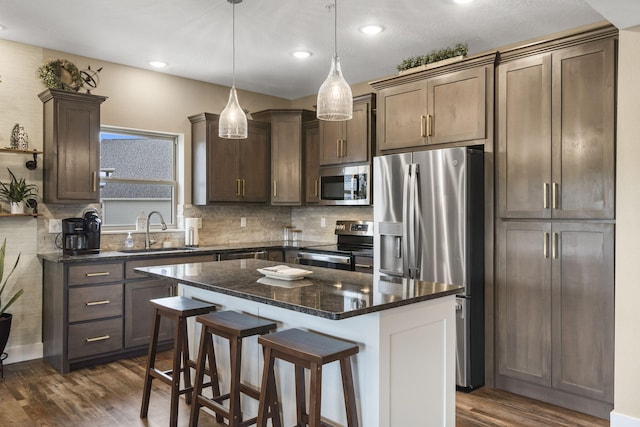 kitchen featuring stainless steel appliances, a sink, a kitchen island, dark wood-type flooring, and a breakfast bar area