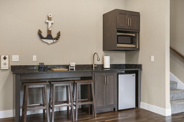 bar featuring stainless steel appliances, a sink, baseboards, stairs, and dark wood-type flooring