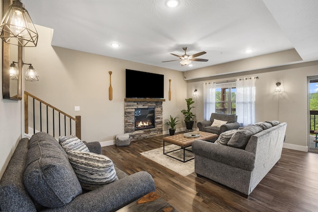 living room featuring ceiling fan, dark hardwood / wood-style flooring, and a stone fireplace