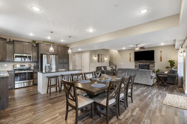 dining space with stairway, a ceiling fan, a fireplace, dark wood-type flooring, and recessed lighting