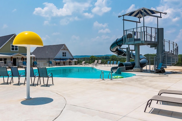 pool featuring a water slide, fence, a patio area, and stairs