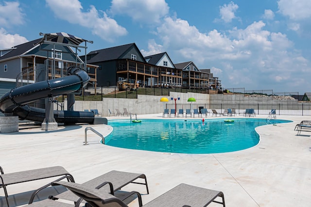 pool featuring a water slide, fence, and a patio area