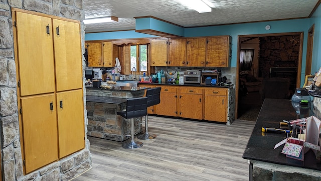 kitchen with sink, ornamental molding, a stone fireplace, a textured ceiling, and light hardwood / wood-style floors