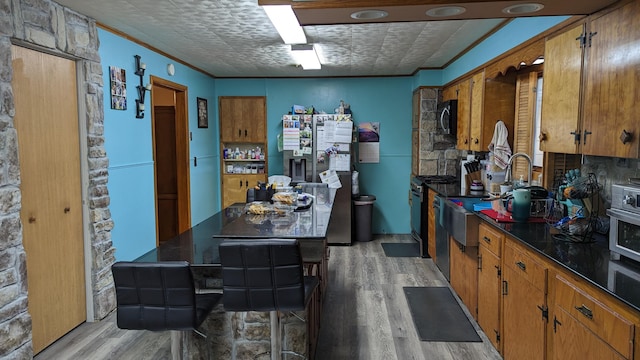 kitchen with appliances with stainless steel finishes, ornamental molding, and light hardwood / wood-style flooring