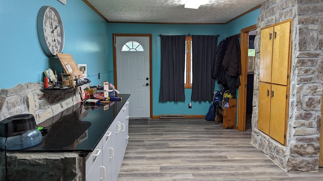 foyer featuring ornamental molding, light wood-type flooring, and a textured ceiling