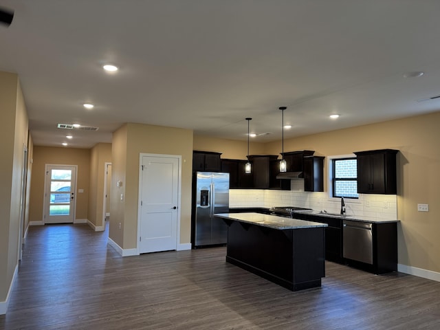 kitchen with appliances with stainless steel finishes, pendant lighting, backsplash, a center island, and light stone counters