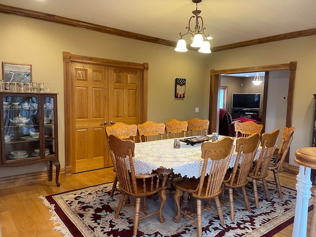 dining area with crown molding, an inviting chandelier, and light hardwood / wood-style flooring