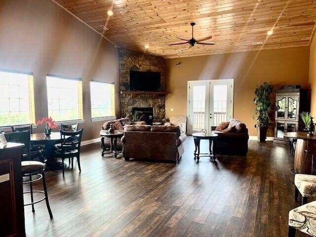 living room with ceiling fan, wooden ceiling, dark wood-type flooring, a towering ceiling, and a fireplace