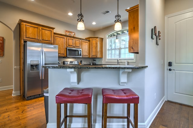 kitchen featuring dark stone counters, a breakfast bar, decorative light fixtures, dark hardwood / wood-style floors, and appliances with stainless steel finishes