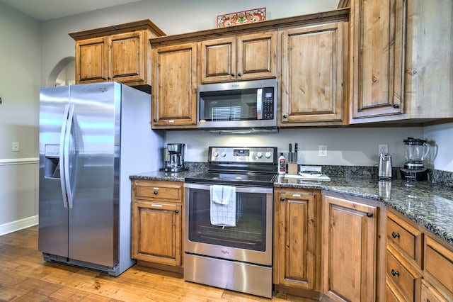 kitchen with stainless steel appliances, light hardwood / wood-style floors, and dark stone counters