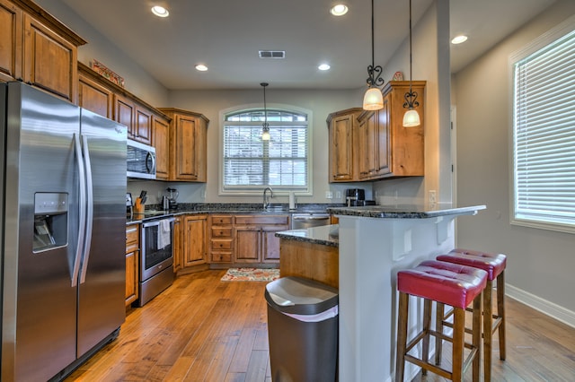 kitchen featuring light hardwood / wood-style flooring, a breakfast bar, dark stone countertops, decorative light fixtures, and stainless steel appliances