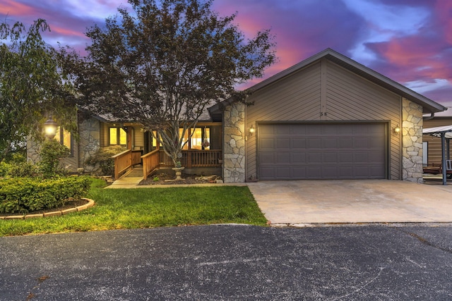 view of front of property featuring a yard, driveway, covered porch, stone siding, and a garage