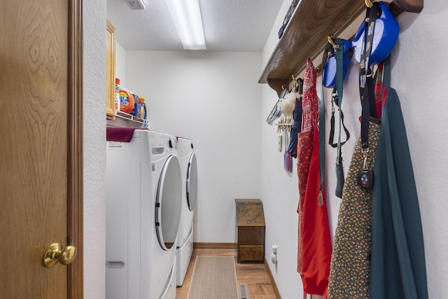 clothes washing area with a textured ceiling, light wood-type flooring, washer and dryer, baseboards, and laundry area