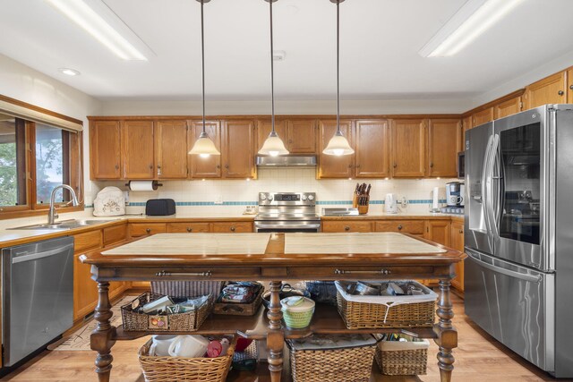 kitchen with stainless steel appliances, a sink, light wood-style floors, light countertops, and under cabinet range hood