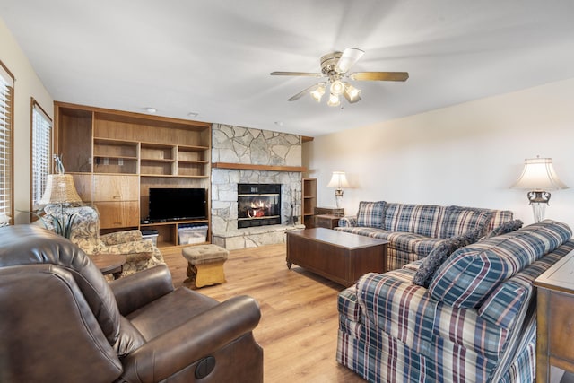 living room with ceiling fan, built in features, a stone fireplace, and wood-type flooring