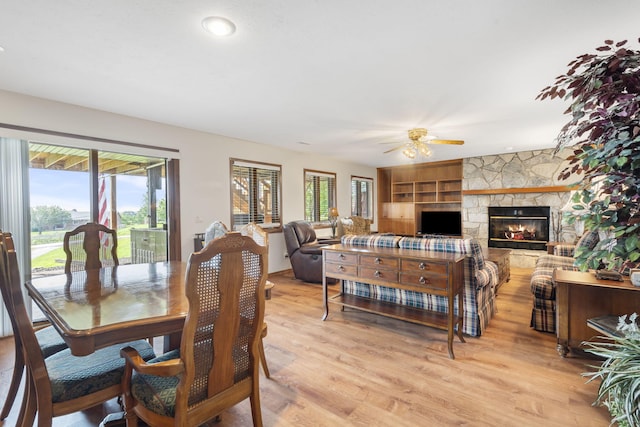 dining area featuring built in features, light hardwood / wood-style floors, a stone fireplace, and ceiling fan