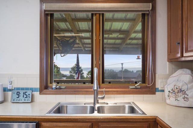 kitchen with light countertops, stainless steel dishwasher, brown cabinetry, a sink, and tasteful backsplash