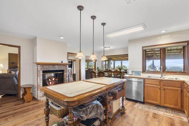 kitchen featuring pendant lighting, sink, stainless steel dishwasher, a fireplace, and light hardwood / wood-style floors