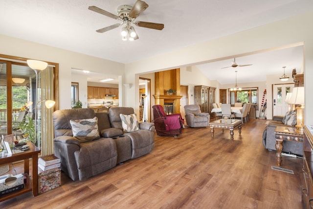 living room with ceiling fan with notable chandelier, hardwood / wood-style flooring, lofted ceiling, and a large fireplace