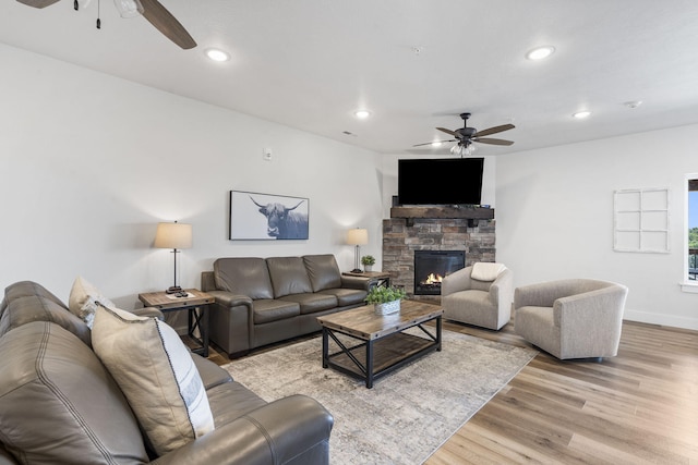 living room with light wood-type flooring, ceiling fan, and a stone fireplace