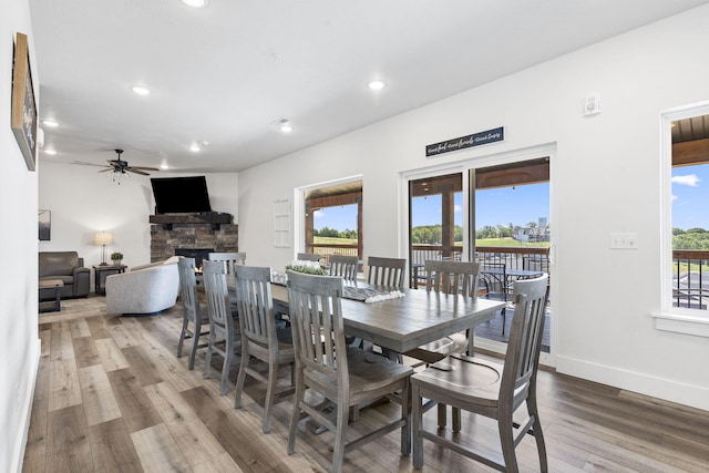 dining area with ceiling fan, a stone fireplace, and hardwood / wood-style flooring