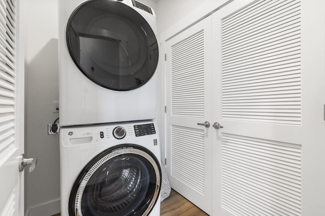 laundry area featuring stacked washer / drying machine and dark wood-type flooring