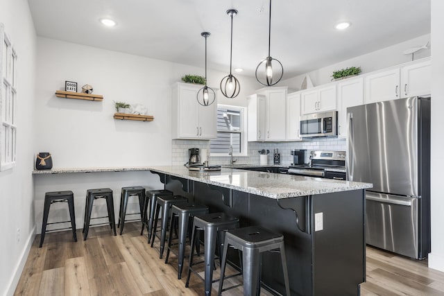 kitchen featuring white cabinets, hanging light fixtures, kitchen peninsula, stainless steel appliances, and light wood-type flooring