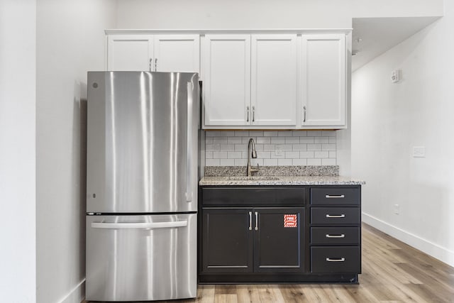 kitchen featuring white cabinets, stainless steel refrigerator, light hardwood / wood-style flooring, and decorative backsplash