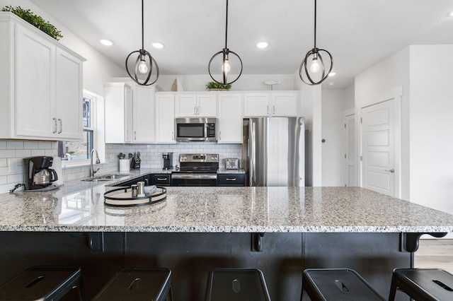 kitchen with decorative light fixtures, sink, appliances with stainless steel finishes, a kitchen bar, and white cabinetry