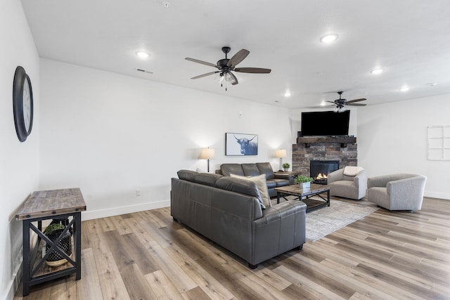 living room with light wood-type flooring, ceiling fan, and a stone fireplace