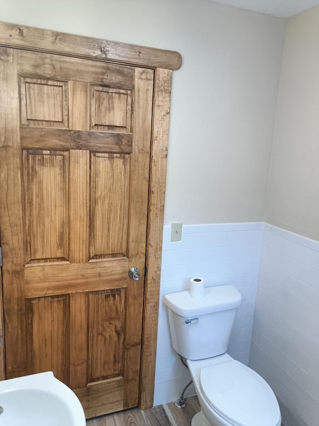 bathroom with toilet, a wainscoted wall, wood finished floors, and tile walls