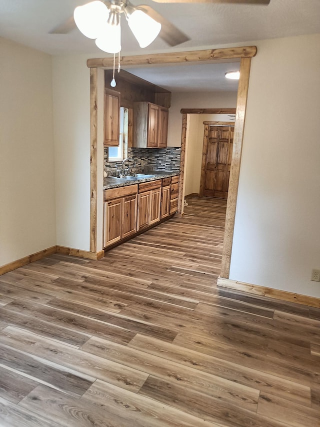 kitchen with dark countertops, wood finished floors, a ceiling fan, and baseboards