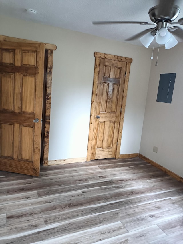spare room with light wood-type flooring, electric panel, a ceiling fan, and baseboards
