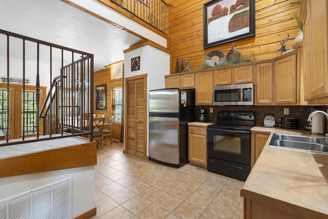 kitchen with a high ceiling, wood walls, sink, and stainless steel appliances